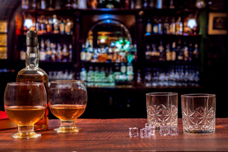 Whiskey bottle, brandy glasses, crystal tumblers and ice cubes on a wooden Irish pub bar with blurred bottles and warm nightlife atmosphere.